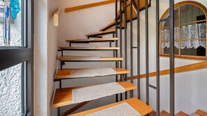Una escalera de madera con barandillas de metal, que lleva a un rellano con un ventanal y una puerta con cortina.