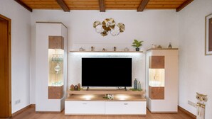 Una sala de estar moderna con un televisor de pantalla plana grande, piso de madera, estanterías empotradas y arte decorativo en la pared.