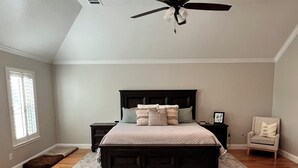A bedroom with a dark wooden bed, a ceiling fan, a light fixture, a window with blinds, a chair, and a rug.