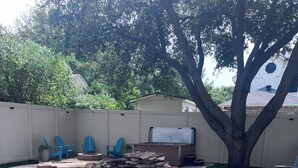 A backyard with a swimming pool, blue chairs, a hot tub, and a large tree.