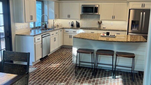 A modern kitchen with white cabinets, a stainless steel refrigerator, and a brick-patterned floor.