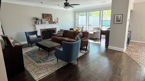 A spacious living room with a fireplace, a ceiling fan, and a large window providing natural light.