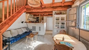 Um interior acolhedor com uma escadaria de madeira, área de jantar com mesa e cadeiras, cozinha e um espaço de estar com sofá e almofadas.
