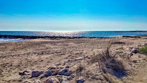 Uma praia arenosa com costa rochosa e céu azul límpido.