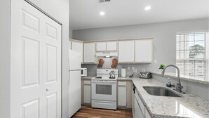A kitchen with white cabinets, a stove, a microwave, and a sink.