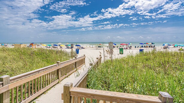 A wooden boardwalk leading to a beach with umbrellas and beach chairs.