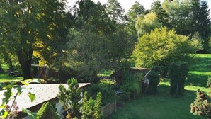 Un jardin agrémenté d’une terrasse en bois, d’un petit abri de jardin et d’une variété d’arbres et d’arbustes.