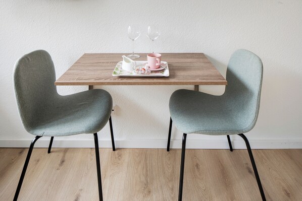 A dining table with two chairs, a tray with a pink cup and a white pitcher, and two empty wine glasses on the wall.