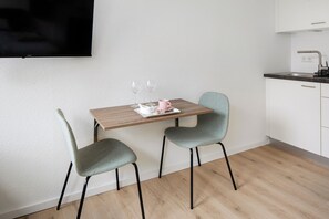 A small kitchenette with a wooden table and two chairs, a television mounted on the wall, and a sink.