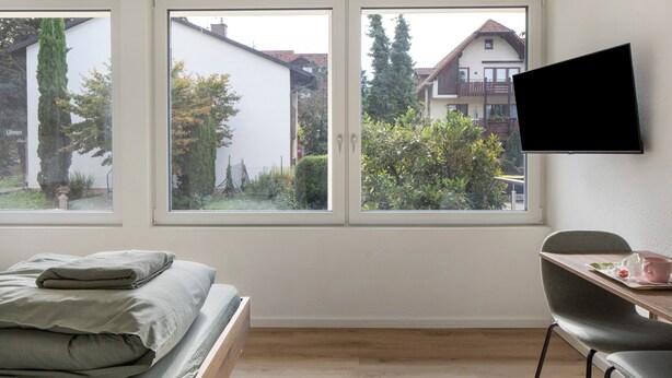 Een slaapkamer met een bed, een bureau, een stoel en een aan de muur bevestigde televisie.