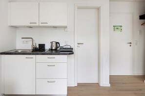 A compact kitchen with white cabinets, a black countertop, and a kettle.