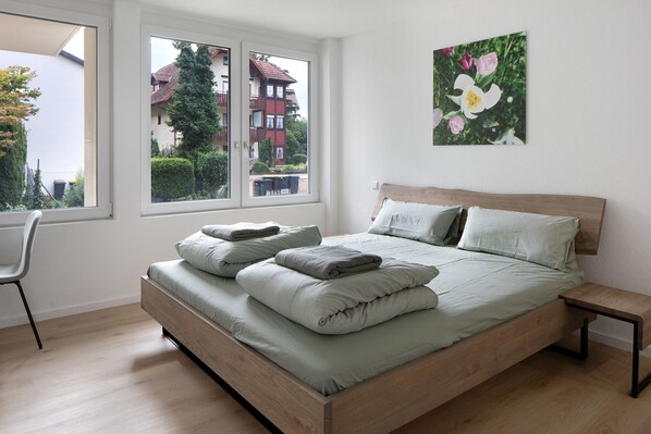 Une chambre à coucher avec un lit, une chaise, une fenêtre et un tableau accroché au mur.
