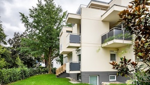Un immeuble résidentiel à plusieurs étages, doté de balcons, d’une pelouse verdoyante et d’arbres matures.