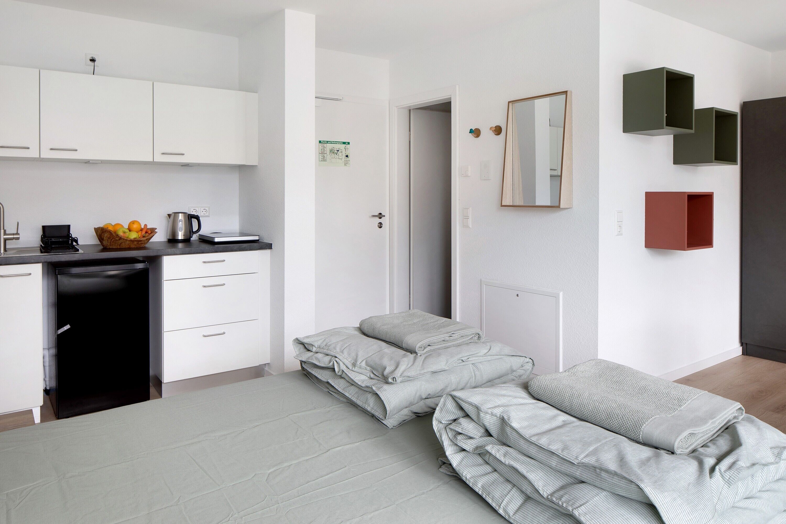 A modern bedroom with a neatly made bed, a small bedside table, and a wall-mounted mirror.