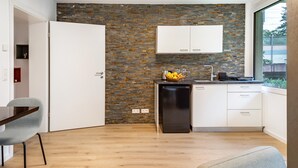 Una cocina moderna con salpicadero de ladrillo, muebles blancos y una zona de comedor con una silla gris.
