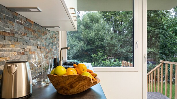 Una cocina con salpicadero de piedra, un cuenco de madera con frutas, una tetera y copas de vino.