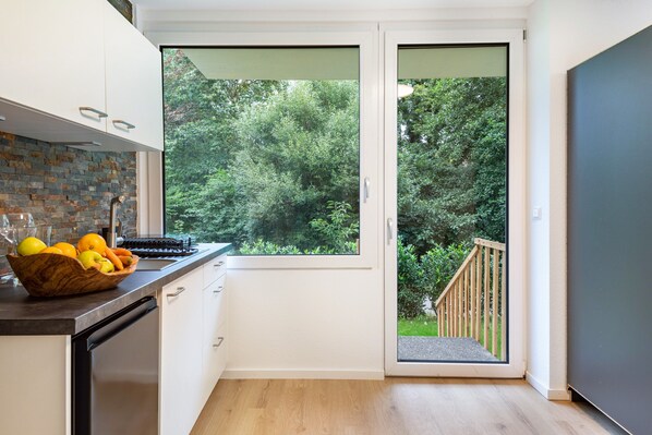 Una cocina moderna con un ventanal grande, una terraza de madera y lavavajillas integrado.