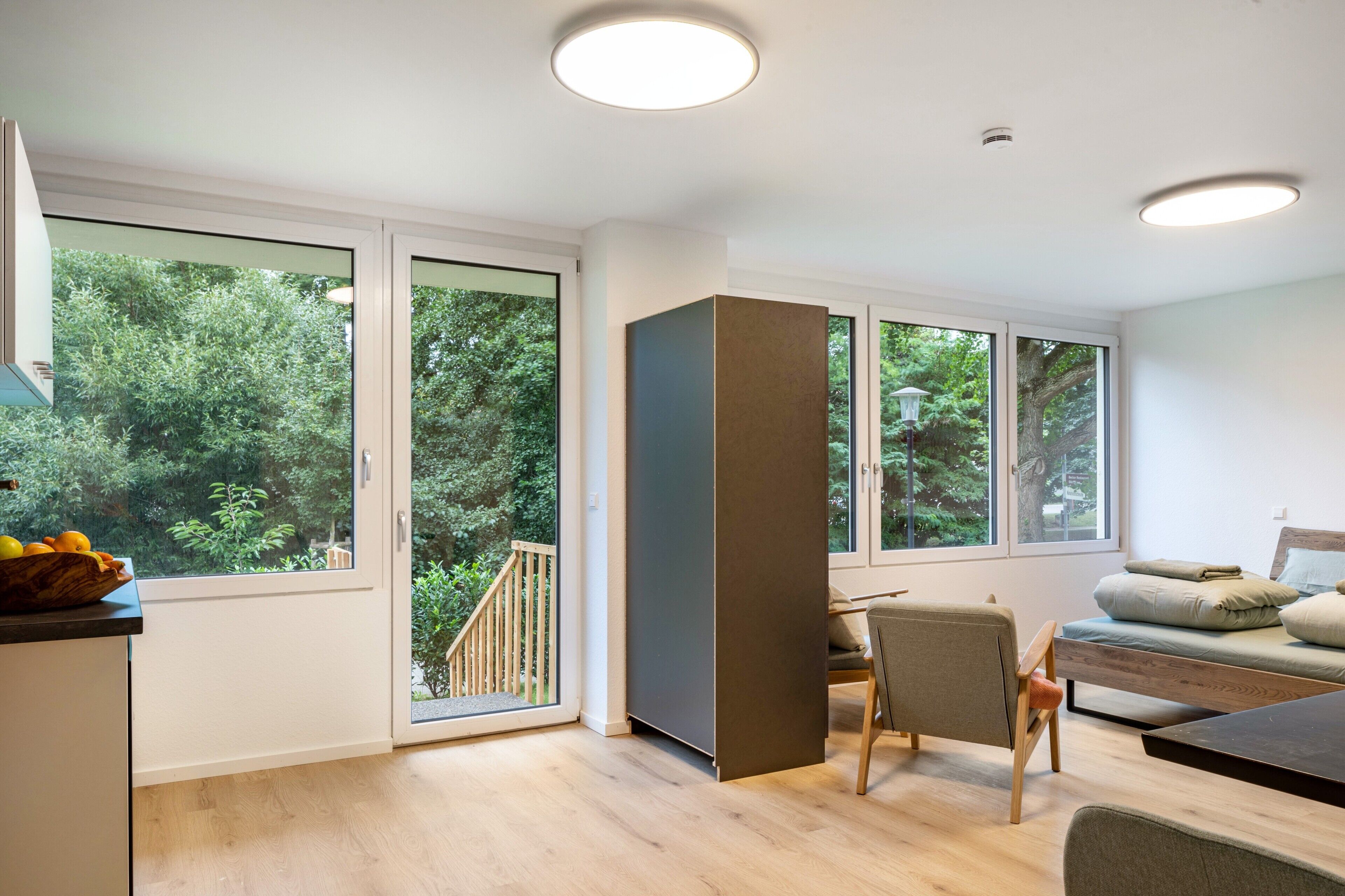 Een moderne kamer met grote ramen, een eethoek en uitzicht op groen.