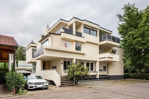 Un edificio residenziale a più piani con balconi, un'auto parcheggiata davanti e un piccolo albero nel vialetto.