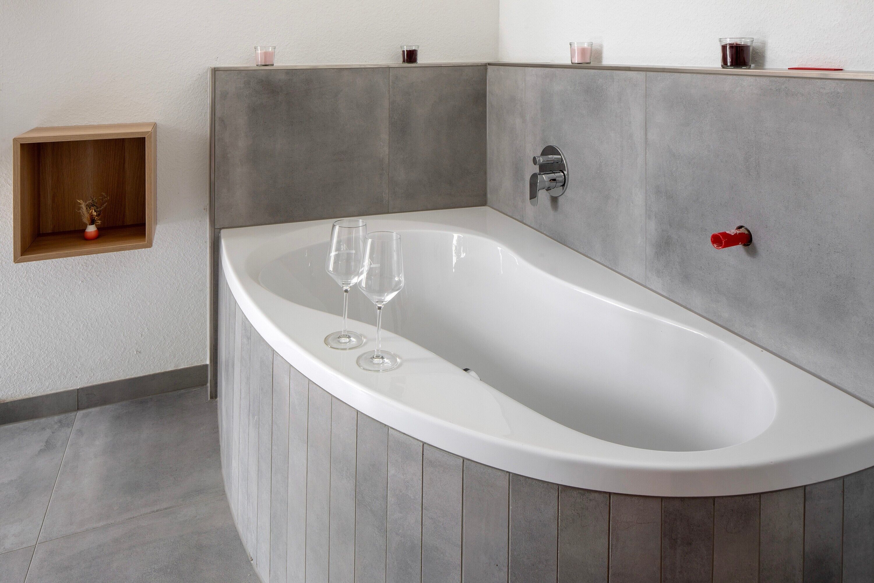 Une salle de bain moderne avec une baignoire sur pieds, une étagère en bois ornée d’un vase et une petite étagère avec des bougies.