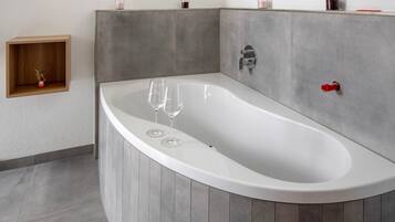 Une salle de bain moderne avec une baignoire sur pieds, une étagère en bois ornée d’un vase et une petite étagère avec des bougies.