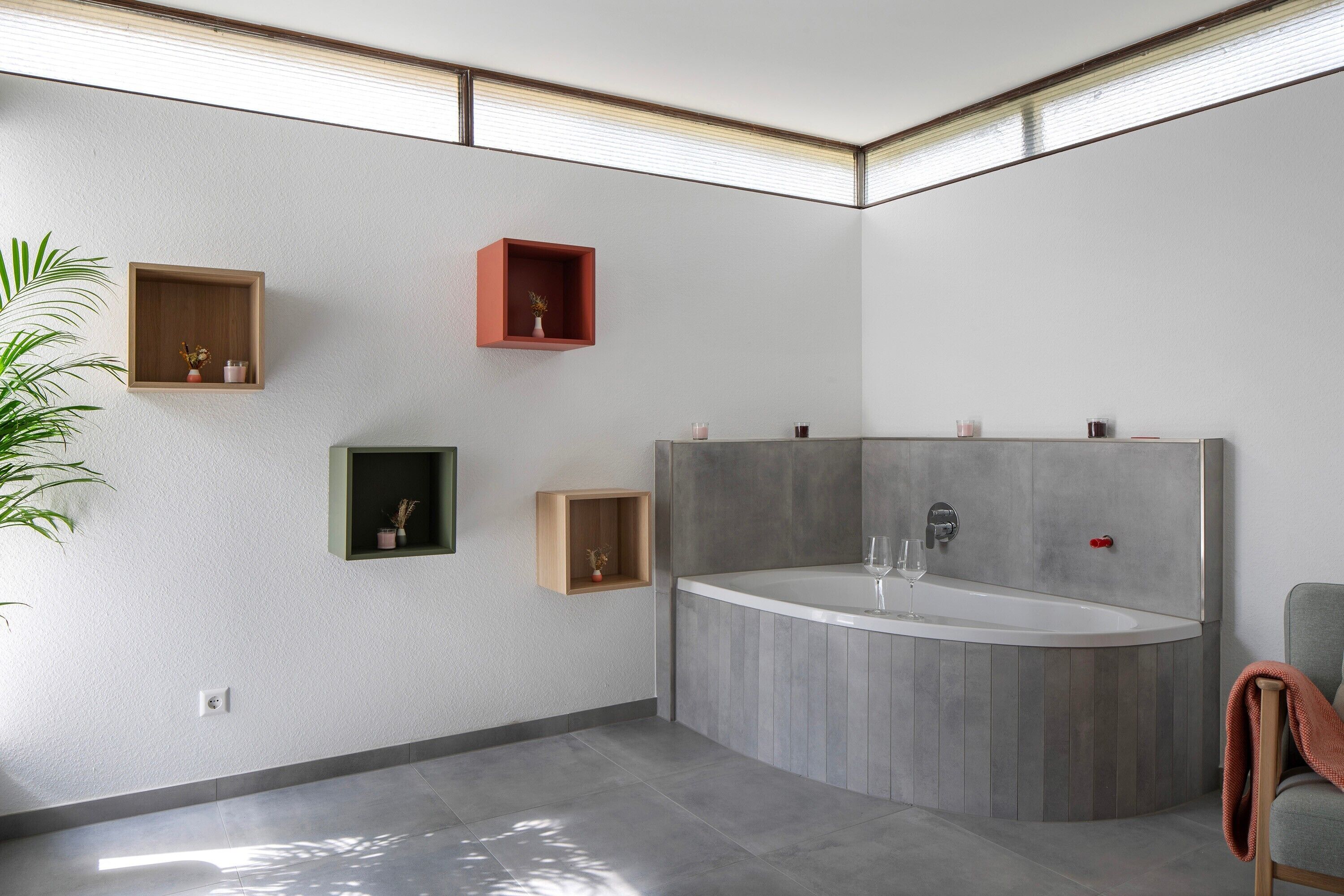 Een moderne badkamer met een vrijstaand bad, inbouwplanken en een potplant.