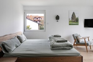 Ein Schlafzimmer mit einem Bett, einem Sessel, einem Fenster, einer Wanduhr und einem Fernseher.