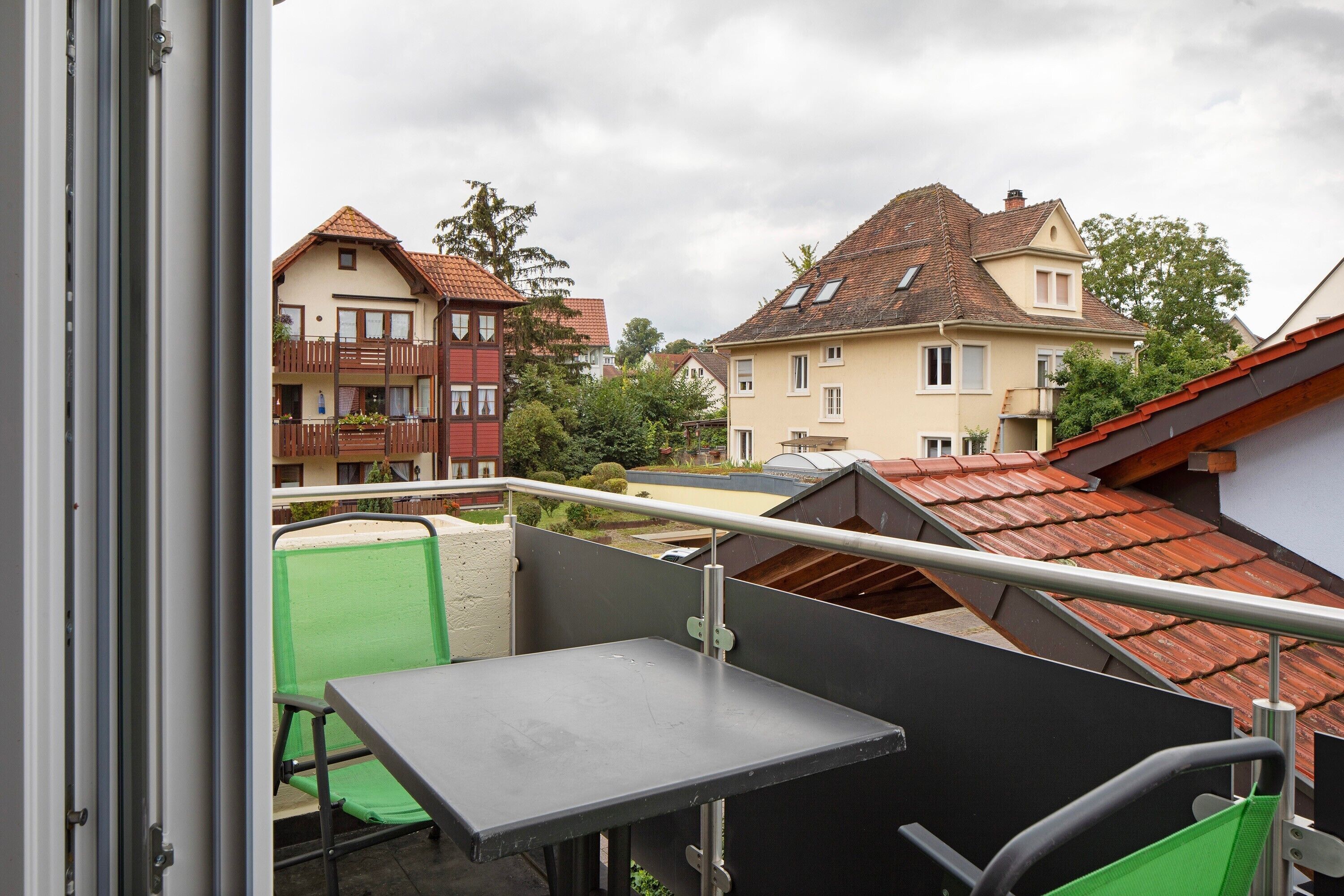 Un balcón con mesa y sillas, con vistas a una zona residencial con casas y un cielo despejado.