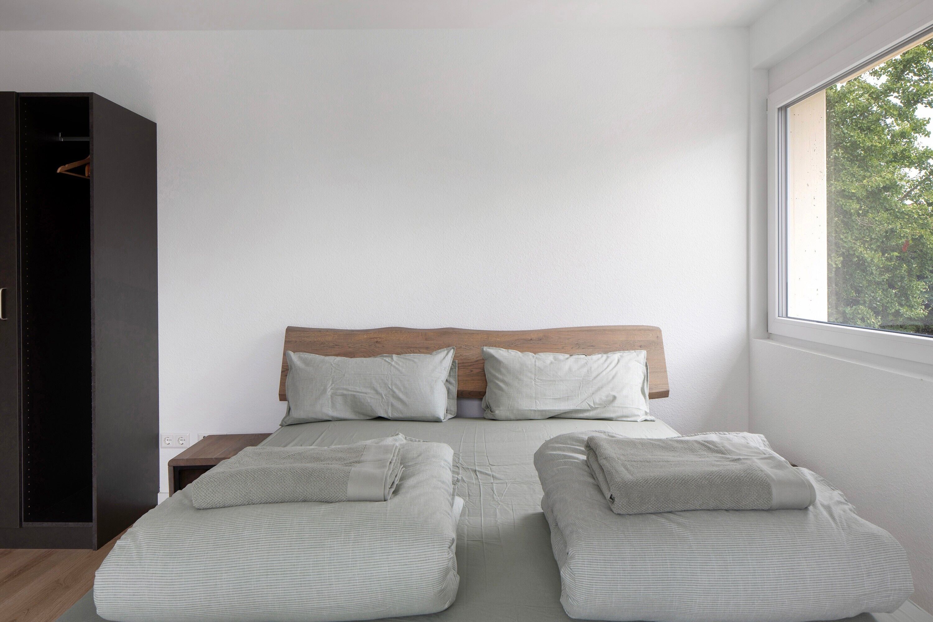 Un dormitorio con cama, dos almohadas, cabecera de madera, mesita de noche y armario.