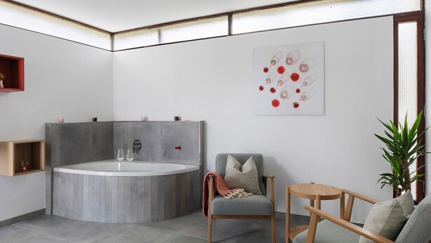 Un baño moderno con una bañera independiente, una silla, una mesita pequeña y una planta en maceta.