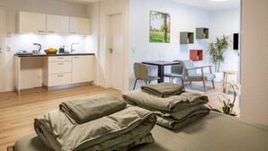 A modern hotel room with a bed, a small desk, a chair, a dining table, and a kitchen area. - Studio Apartment 'Belchen' with balcony and Wi-Fi (Bad Krozingen)
