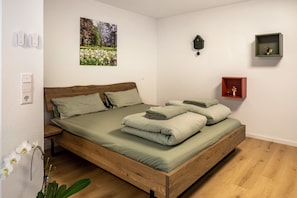 Una camera da letto con un letto in legno, un quadro appeso al muro, un piccolo ripiano e una presa elettrica.