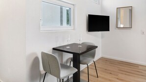 Une chambre moderne équipée d’une table, de deux chaises, d’un téléviseur à écran plat, d’un miroir et de deux fenêtres.