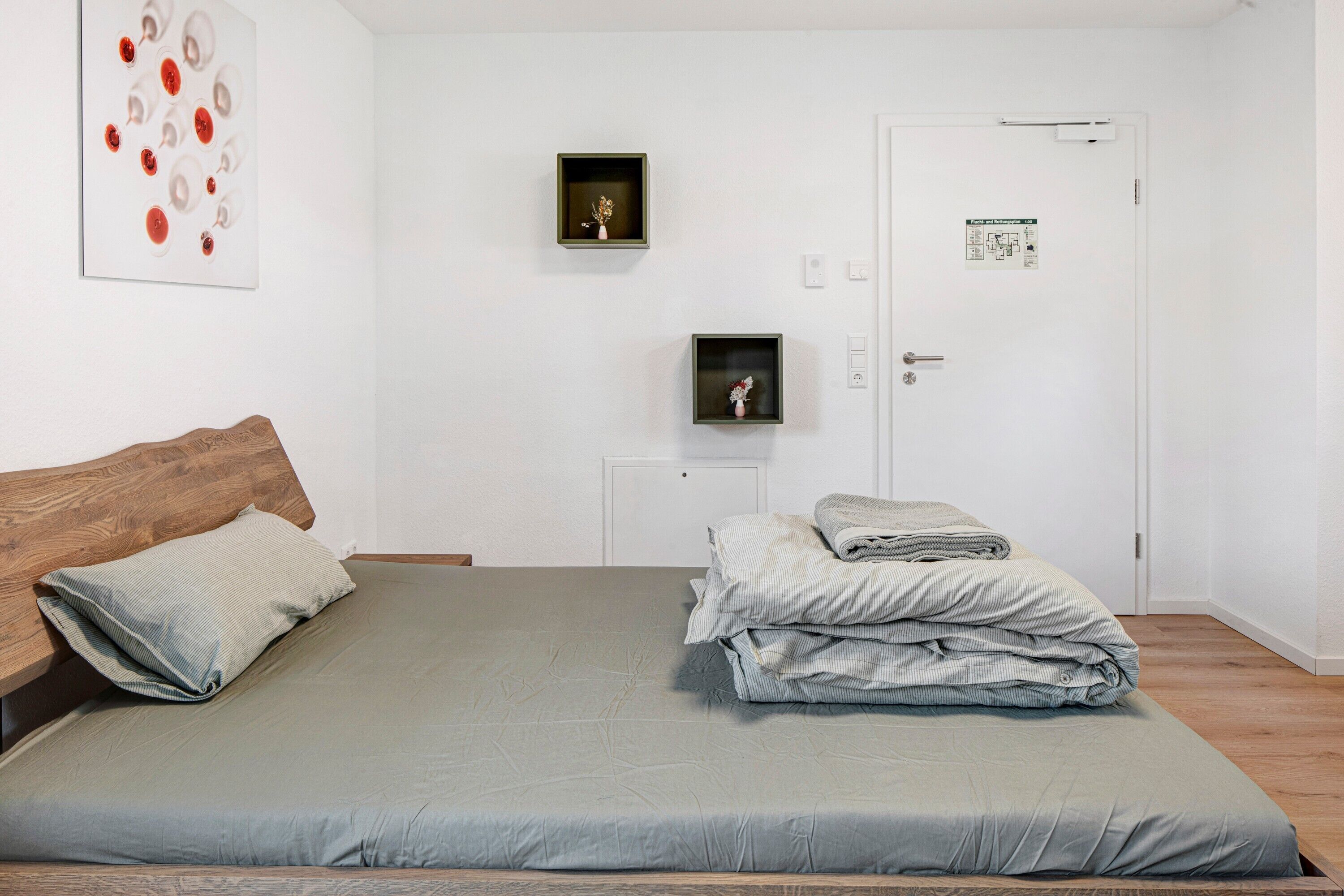 Un dormitorio con una cama, cabecera de madera, un cuadro en la pared y una puerta con un cartel.