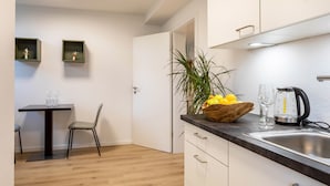 Une cuisine moderne avec une table en bois, une chaise, un saladier de fruits, une machine à café et un évier.