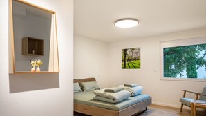Une chambre à coucher avec un lit, une chaise, une fenêtre, un miroir et un tableau accroché au mur.