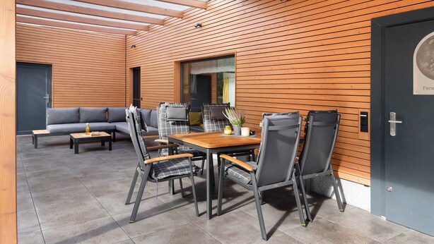 An outdoor seating area with a wooden table and chairs, a sofa, and a window. - Holiday Home 'Mond am See' with Lake View, Private Terrace and Wi-Fi (Stechow-Ferchesar)
