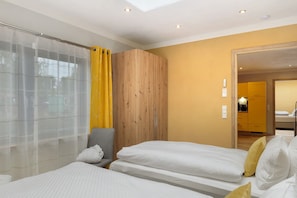 A bedroom with two beds, a wooden wardrobe, a shower area with yellow curtains, and a mirror reflecting a kitchen area. - Holiday Home 'Mond am See' with Lake View, Private Terrace and Wi-Fi (Stechow-Ferchesar)