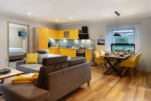 Ein modernes Wohnzimmer mit einer Couch, einem Esstisch mit Stühlen, einer Küchenzeile mit gelben Schränken und einem Fenster mit Blick.