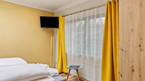 Una habitación de hotel con cama, una mesita, televisión en la pared y cortinas.