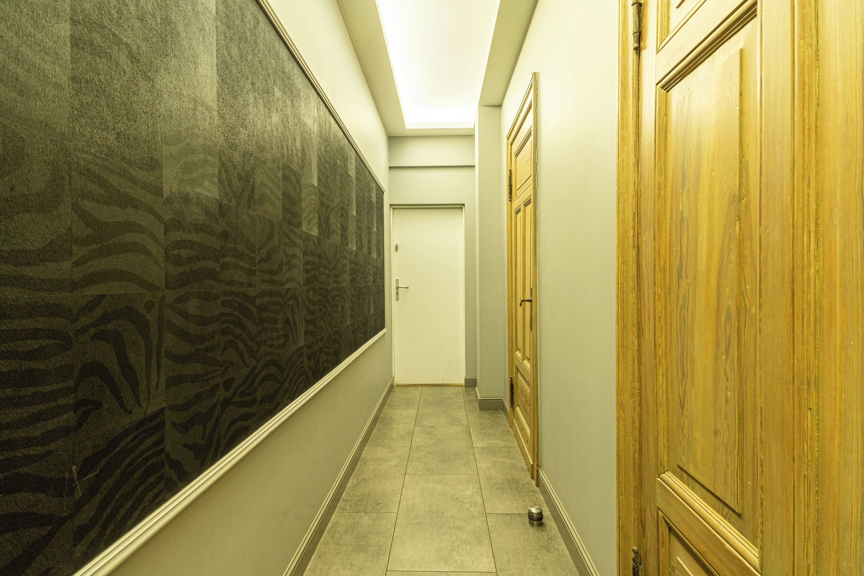 A narrow hallway with patterned wallpaper, a wooden door, and a tiled floor.