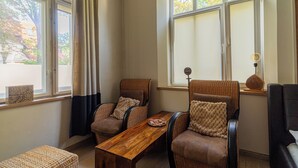 A cozy seating area with wicker chairs, a wooden table, and a view of a garden through large windows. - Africana by Grand Apartments (Sopot)