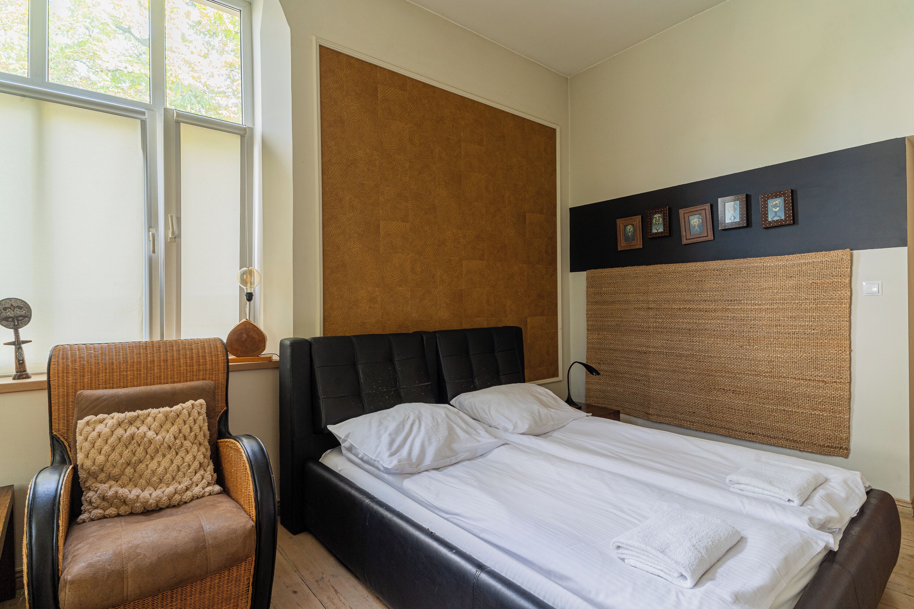 A bedroom with a bed, a chair, a window, and a wall with framed pictures.