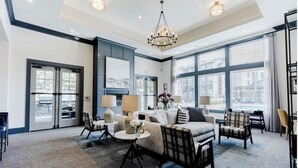 A spacious living room with a large window, a chandelier, and a fireplace.