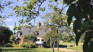 A house with a sloped roof, surrounded by a well-maintained lawn and trees. - Countryside Home Sleeps 6 - Garden, Parking, Wifi (Landivy)