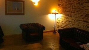 A cozy living room with a stone wall, a leather armchair, a floor lamp, and a framed picture on the wall. - Countryside Home Sleeps 6 - Garden, Parking, Wifi (Landivy)