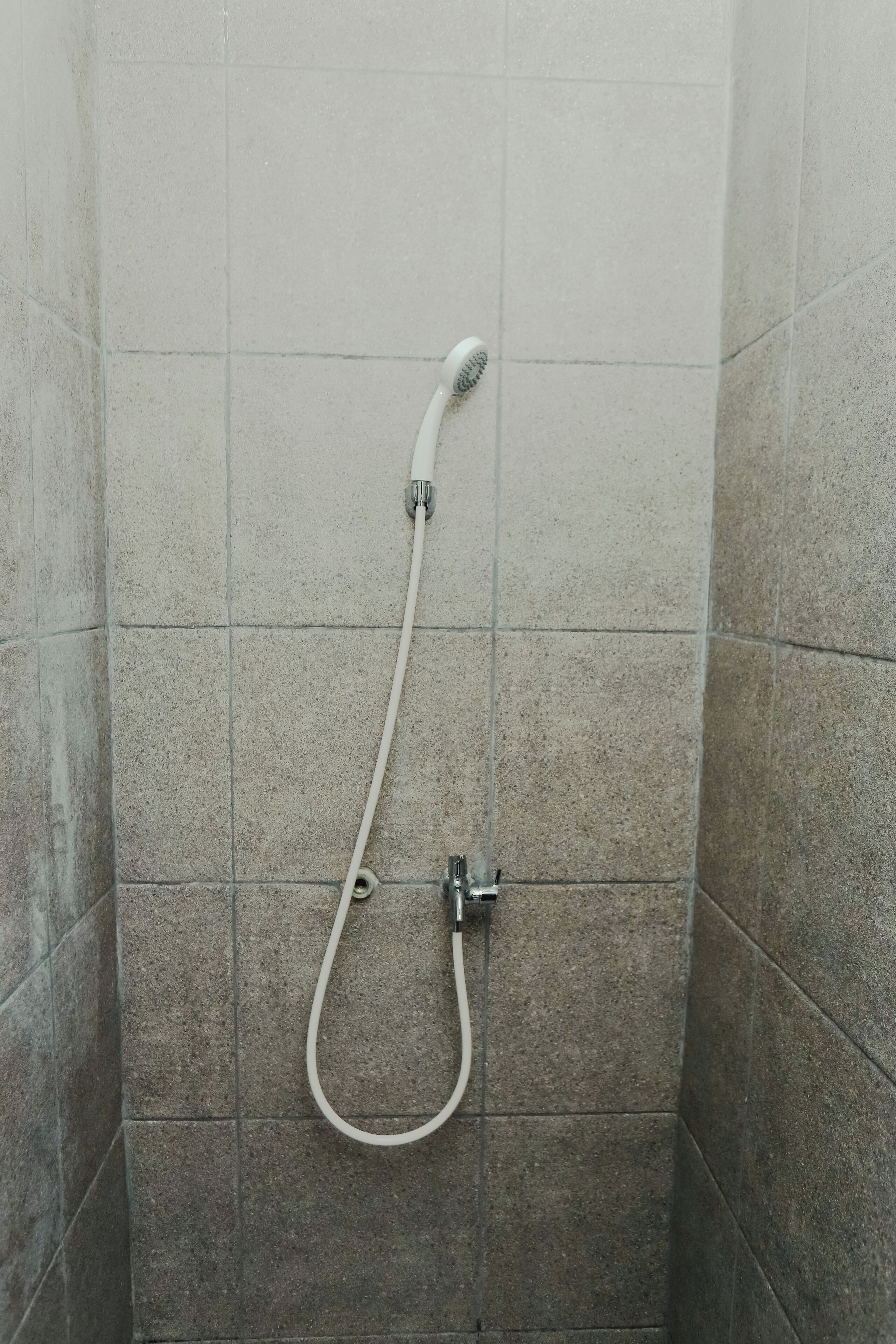 Una ducha con cabezal de mano y grifo empotrado en una habitación con paredes de azulejos.