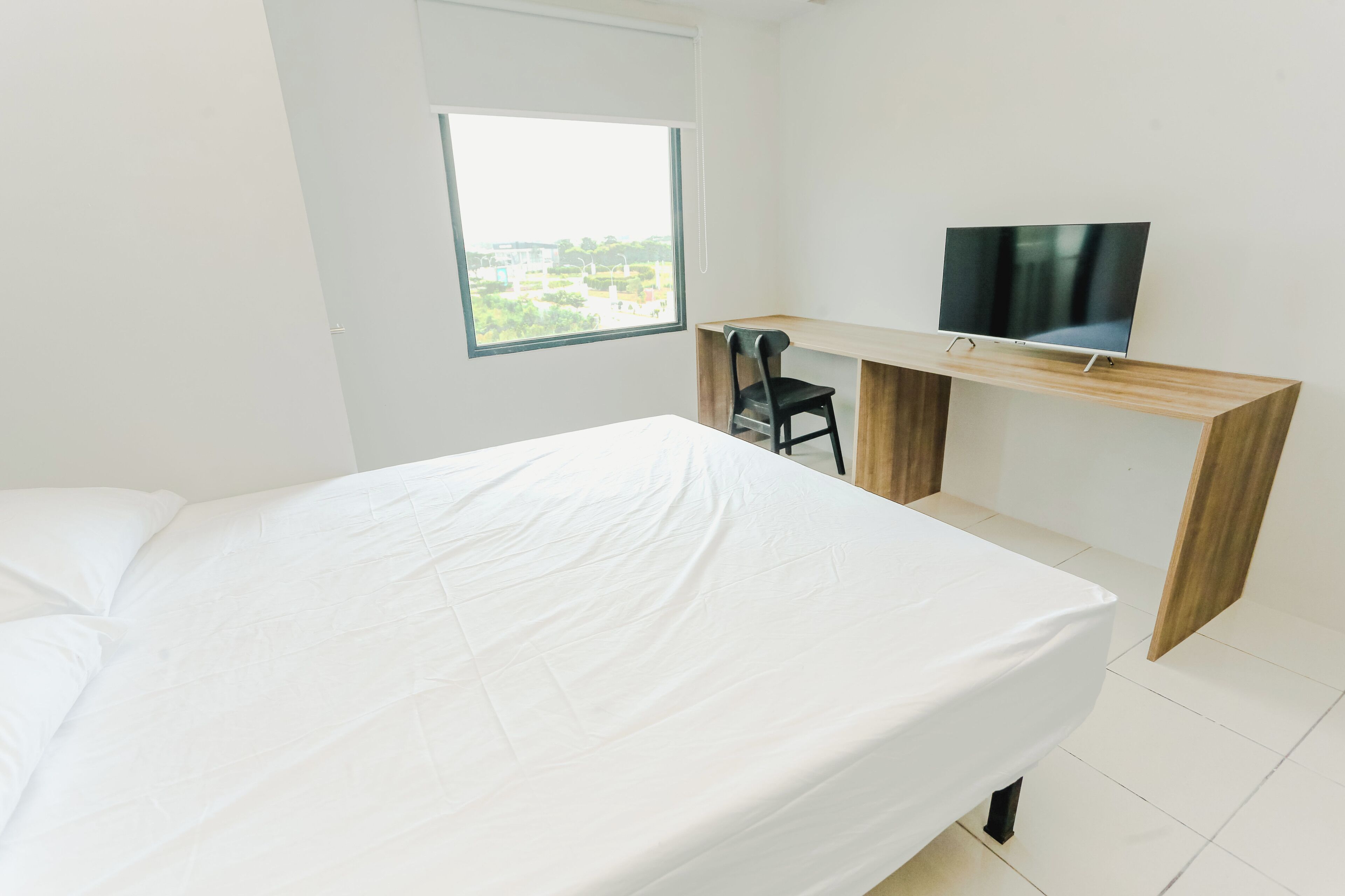 A bedroom with a bed, a desk, a chair, and a TV.