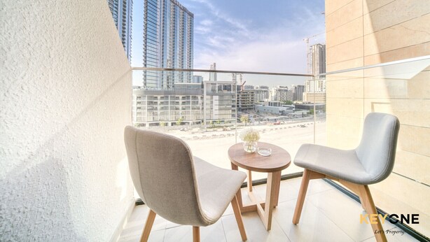 A balcony with two chairs and a small table, overlooking a cityscape with high-rise buildings. - Spacious Azizi Riviera Studio (Dubai)