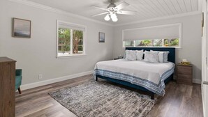 Une chambre à coucher avec un lit, un ventilateur de plafond, une fenêtre et une table de chevet.